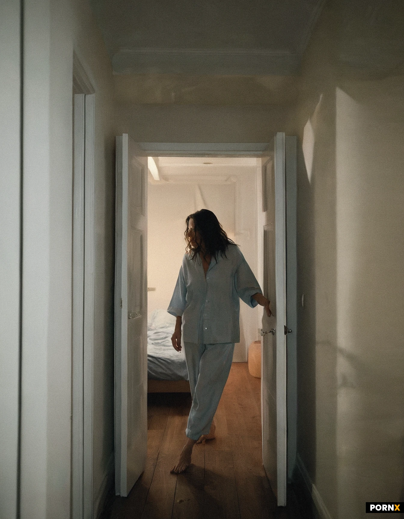 Hyper-realistic cinematic photograph, hot summer night inside a quiet apartment. Sophie, an adult woman in her mid-20s, walks barefoot down a dim hallway toward her roommate’s bedroom. Warm low apartment lighting, slightly tousled bedtime hair, lightweight sleepwear appropriate for a humid summer night, relaxed but curious expression. At the end of the hallway, the bedroom door is slightly open with faint light spilling through the gap. Candid natural moment, realistic skin pores and texture, individual hair strands, authentic fabric wrinkles, physically accurate lighting, 50mm full-frame photography, shallow depth of field, subtle film grain, no CGI appearance.