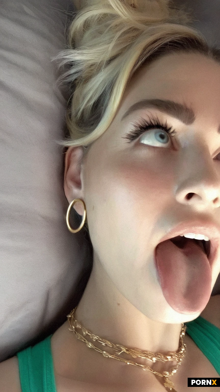 Close-up selfie of a woman with blonde hair styled in a high messy bun, (Ahegao:1.3),20, soft smile showing teeth, long eyelashes, defined eyebrows, small mole on her cheek, wearing large gold hoop earrings and a gold necklace, teal tank top strap visible, warm indoor lighting, photorealistic, highly detailed skin texture and facial features, sharp focus, particle light ,portrait ,cinematic illumination ,volumetric lighting ,wide angle ,hyper realistic ,ultra HD,